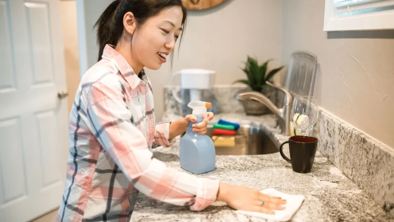 Persona che pulisce il lavello della cucina con uno spray al vinagre e un panno